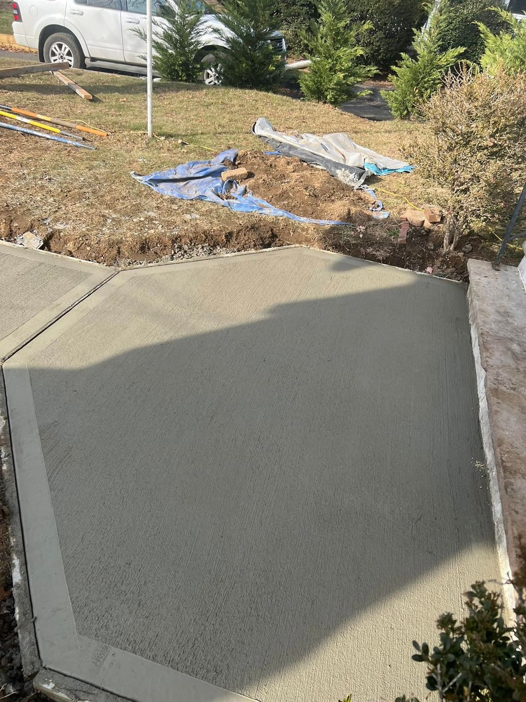 Freshly poured broom-finish concrete walkway beside a driveway.