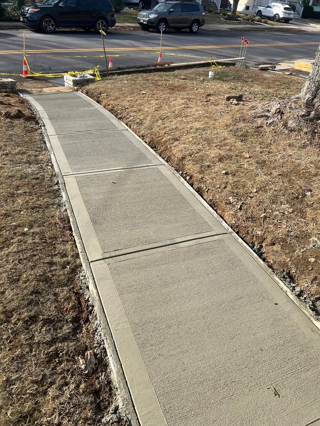 Freshly poured curved concrete front walkway crossing a yard toward a residential street.