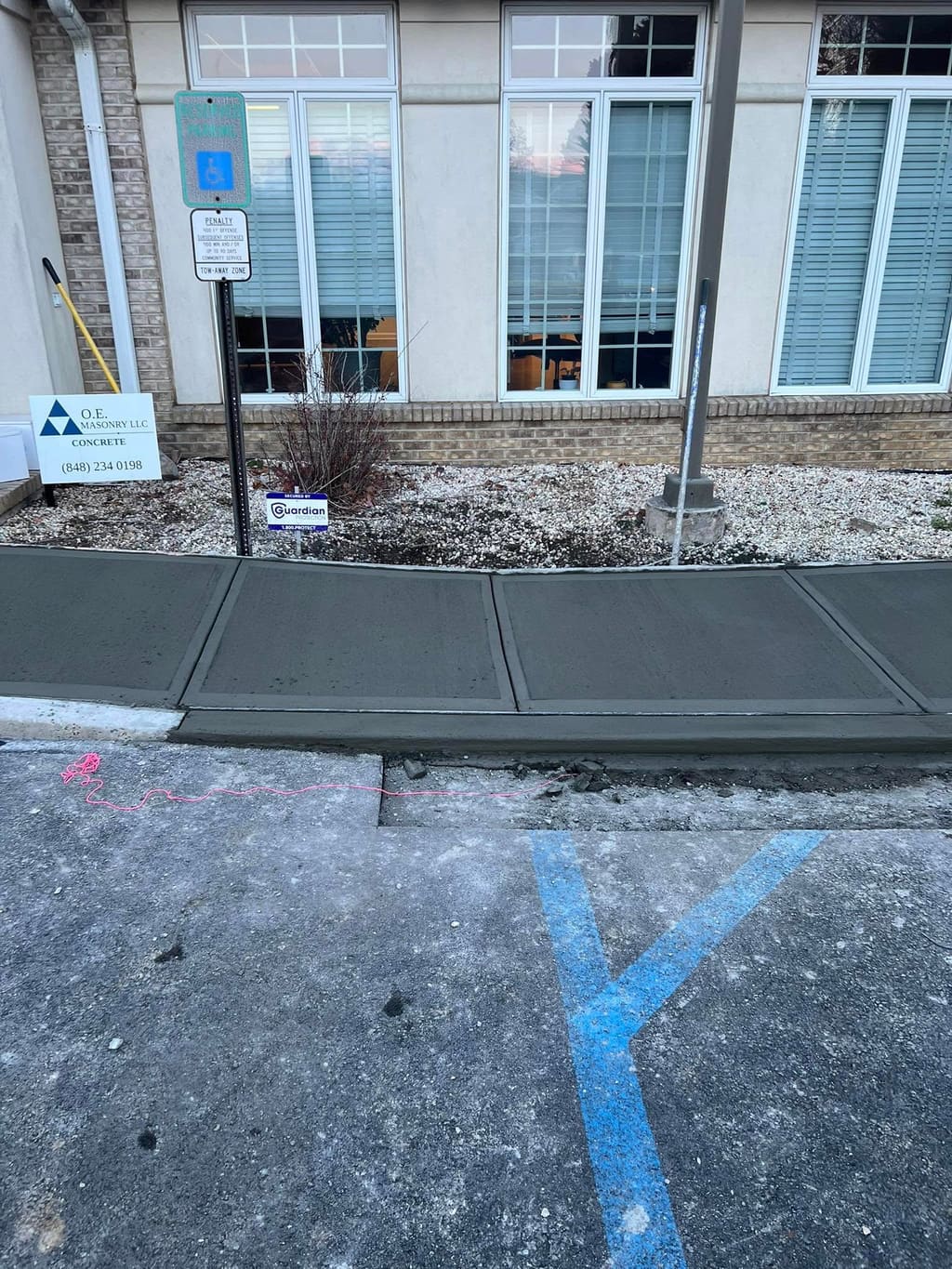 Newly poured concrete walkway section in front of a commercial building beside a parking lot.