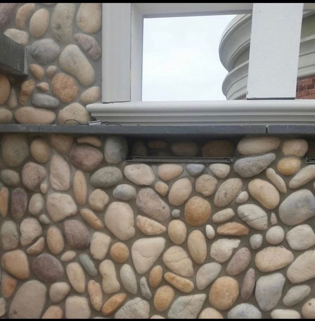 Rounded river-rock stone veneer covering a building's lower wall around a windowsill.