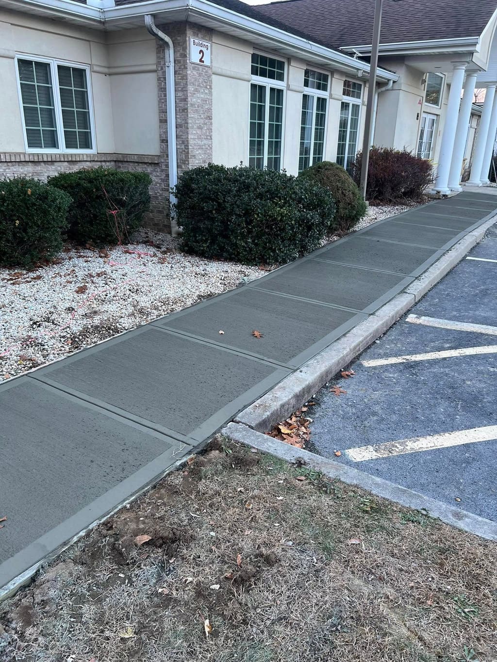 Freshly poured concrete sidewalk running alongside a commercial building beside a parking lot.