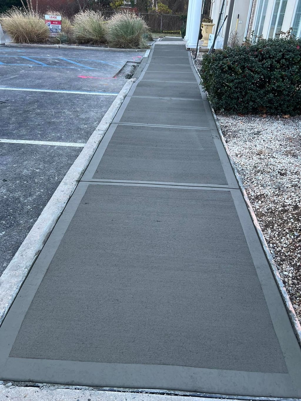 Long broom-finish concrete walkway with darker troweled borders leading to a building entrance.