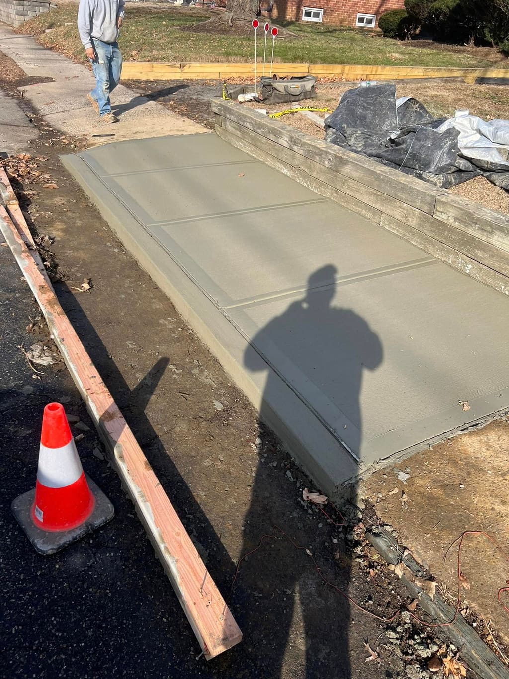 Newly poured and finished concrete driveway slab next to a curb with a safety cone.