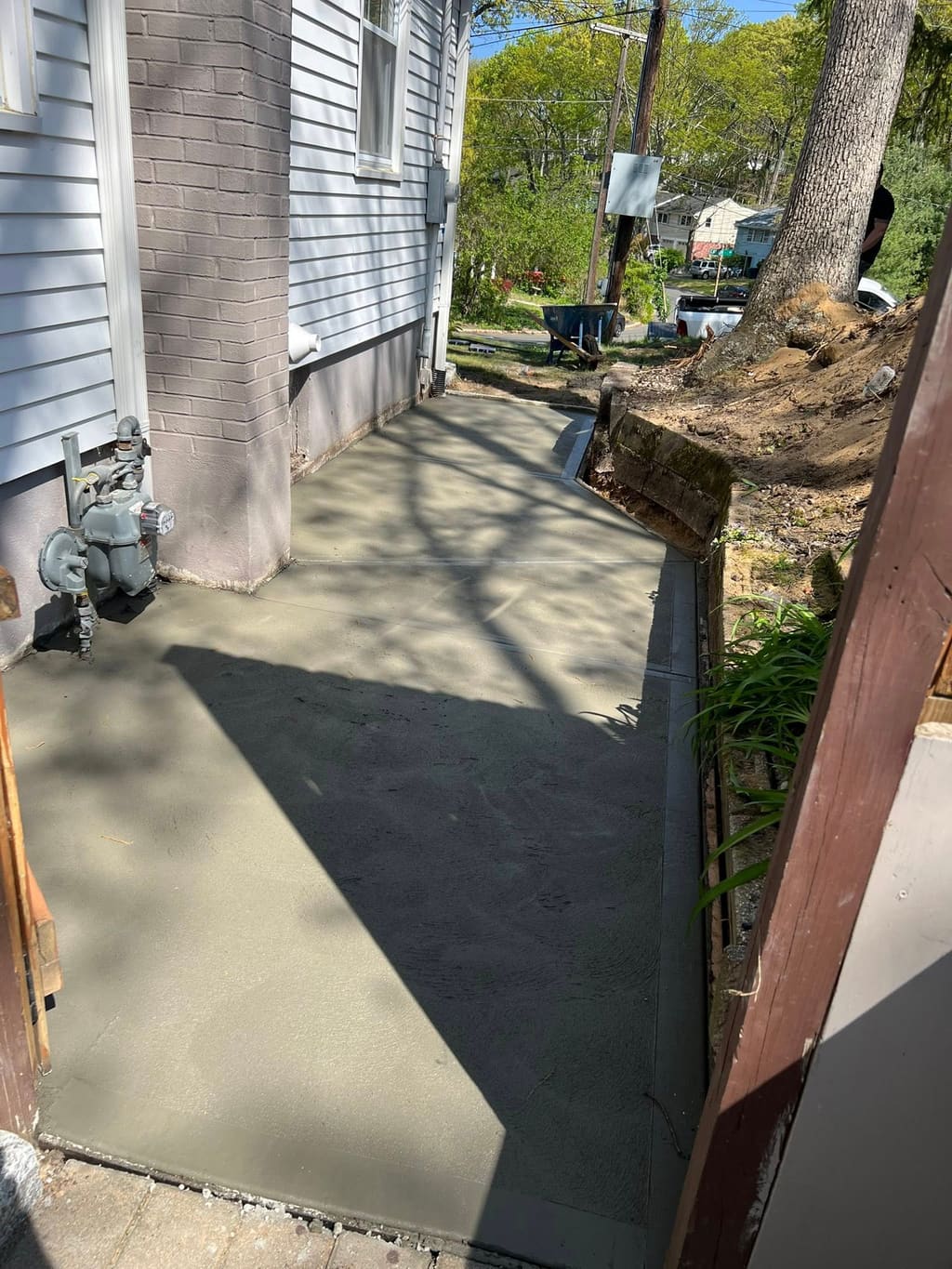 Large freshly poured smooth concrete slab pad running along the side of a sided house.