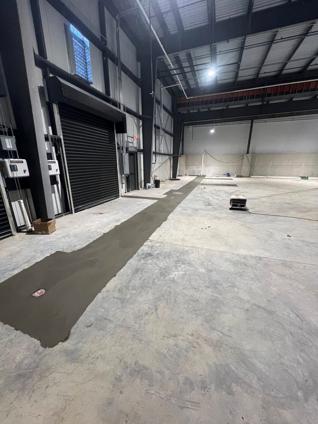 Long strip of fresh concrete slab patched across an existing interior warehouse floor.