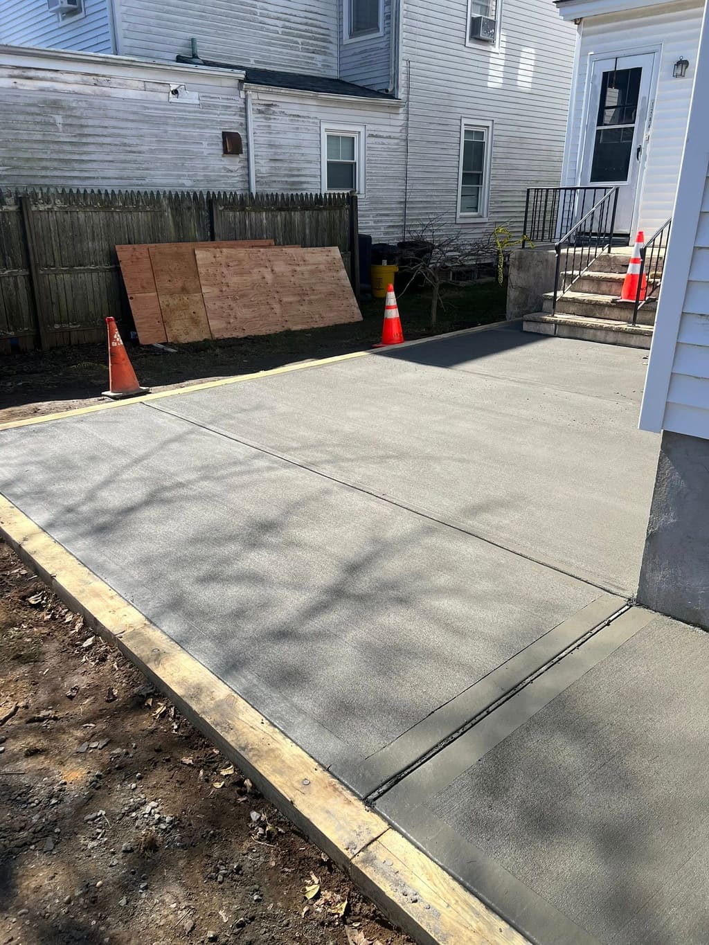 Newly poured concrete patio in a residential backyard with wood forms beside the house entry.