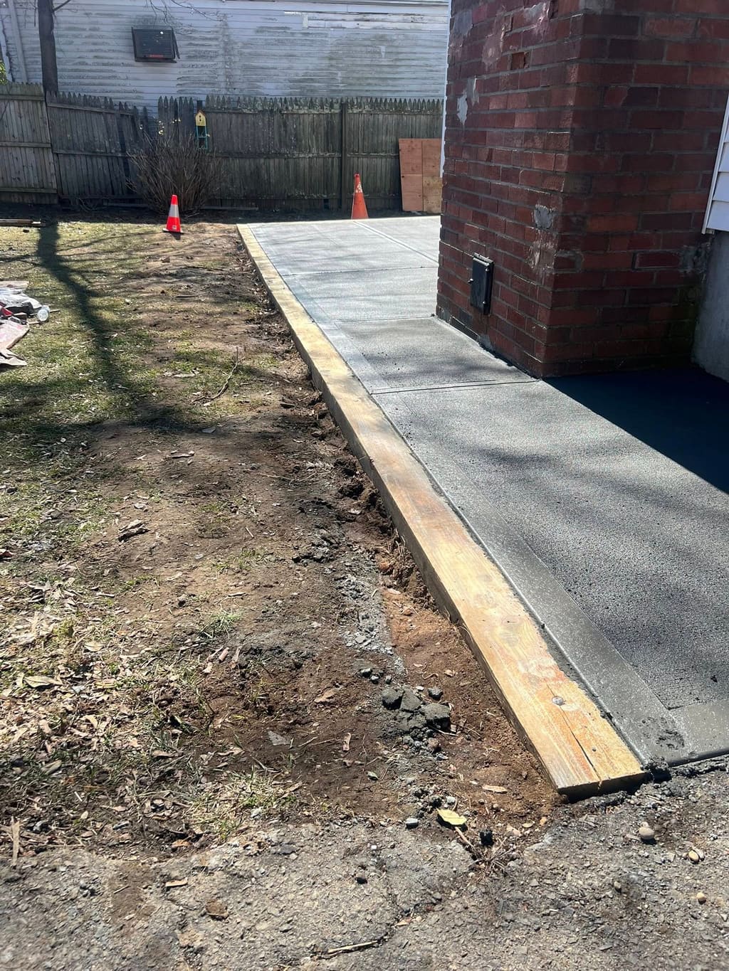Freshly poured concrete walkway strip running alongside a brick building with wood forms in place.