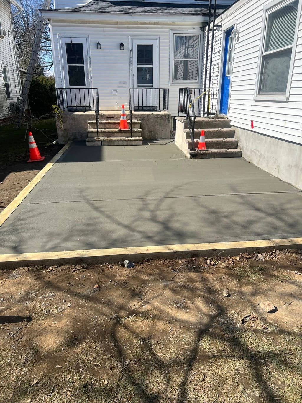 Fresh concrete patio behind a house leading up to masonry steps and a rear stoop.