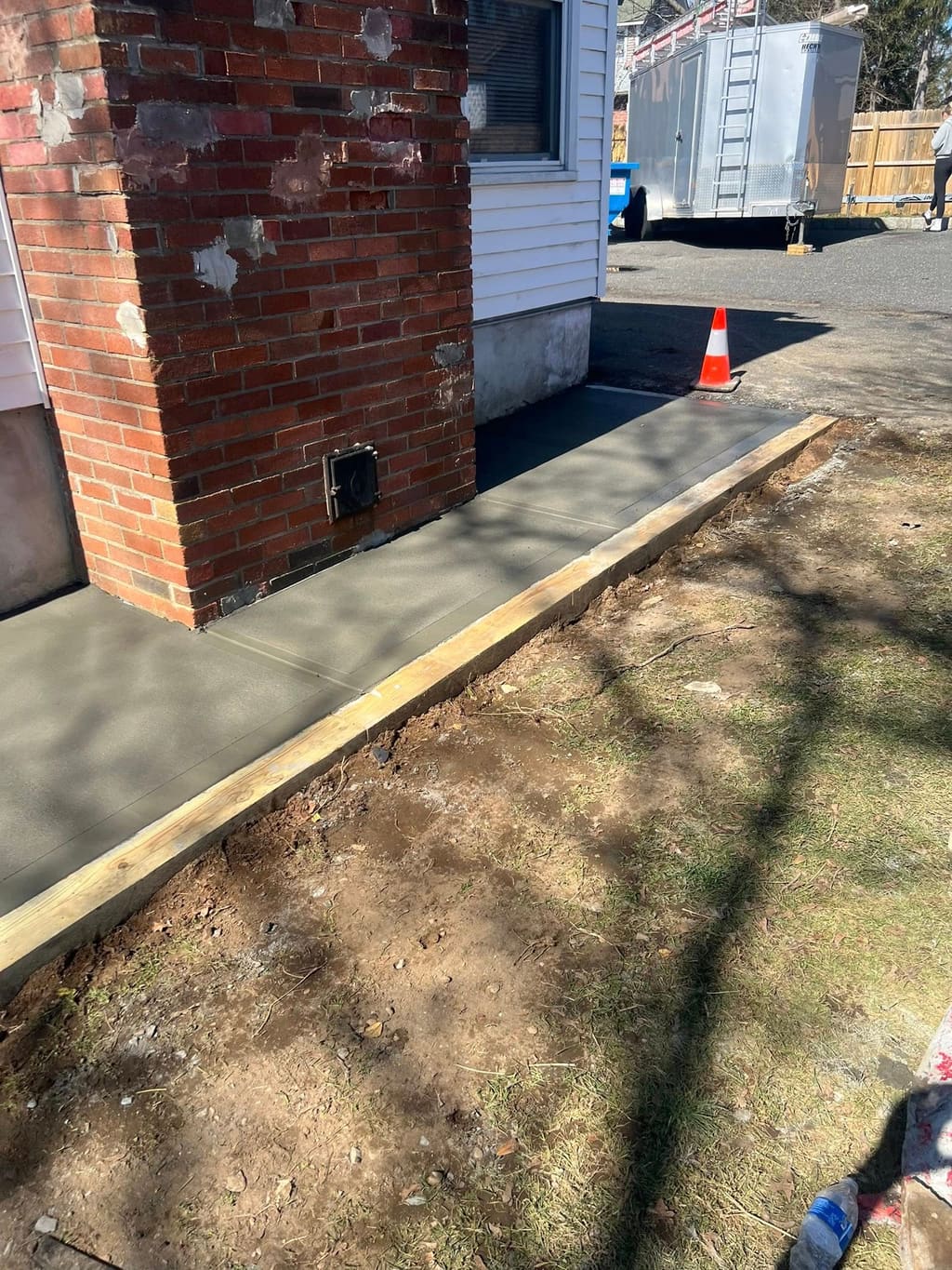 Fresh light-gray concrete walkway poured along the side of a house past a brick chimney.