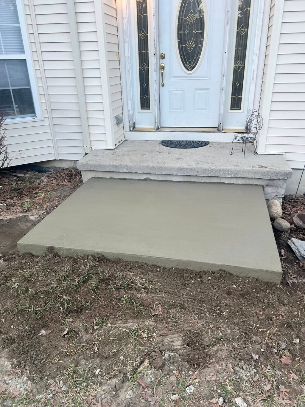 Freshly poured smooth concrete landing pad at a front door beneath an existing concrete stoop.