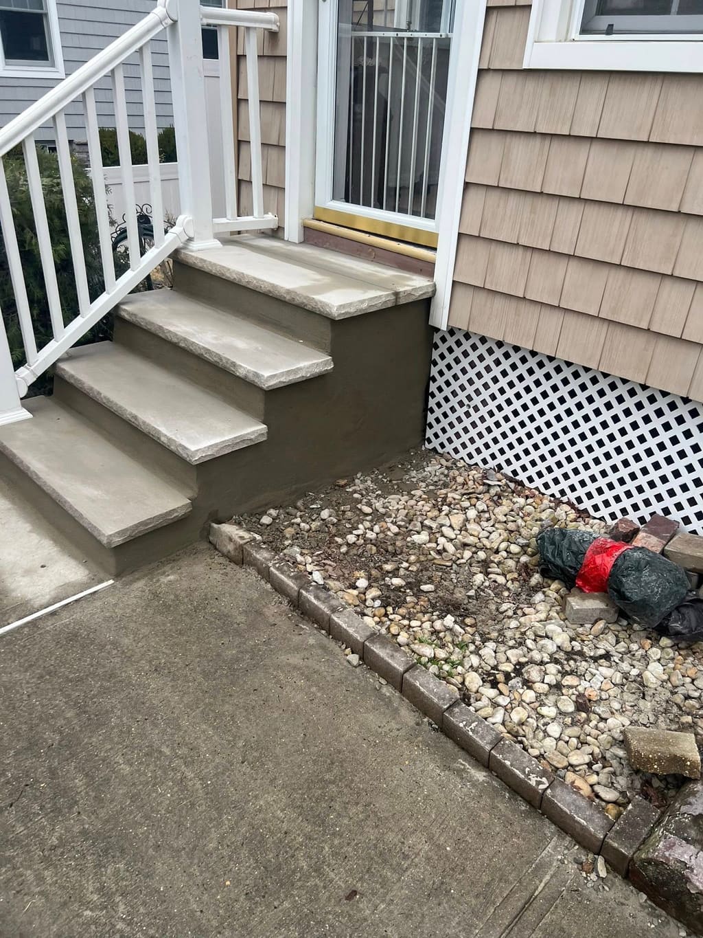Rebuilt concrete entry steps with smooth parged risers beside a brick-edged river-rock bed.