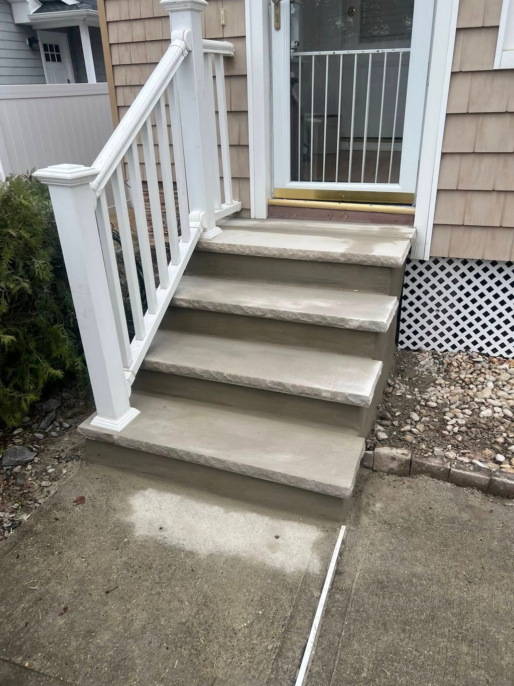 Finished concrete front steps with rock-faced tread edges and a white vinyl railing.