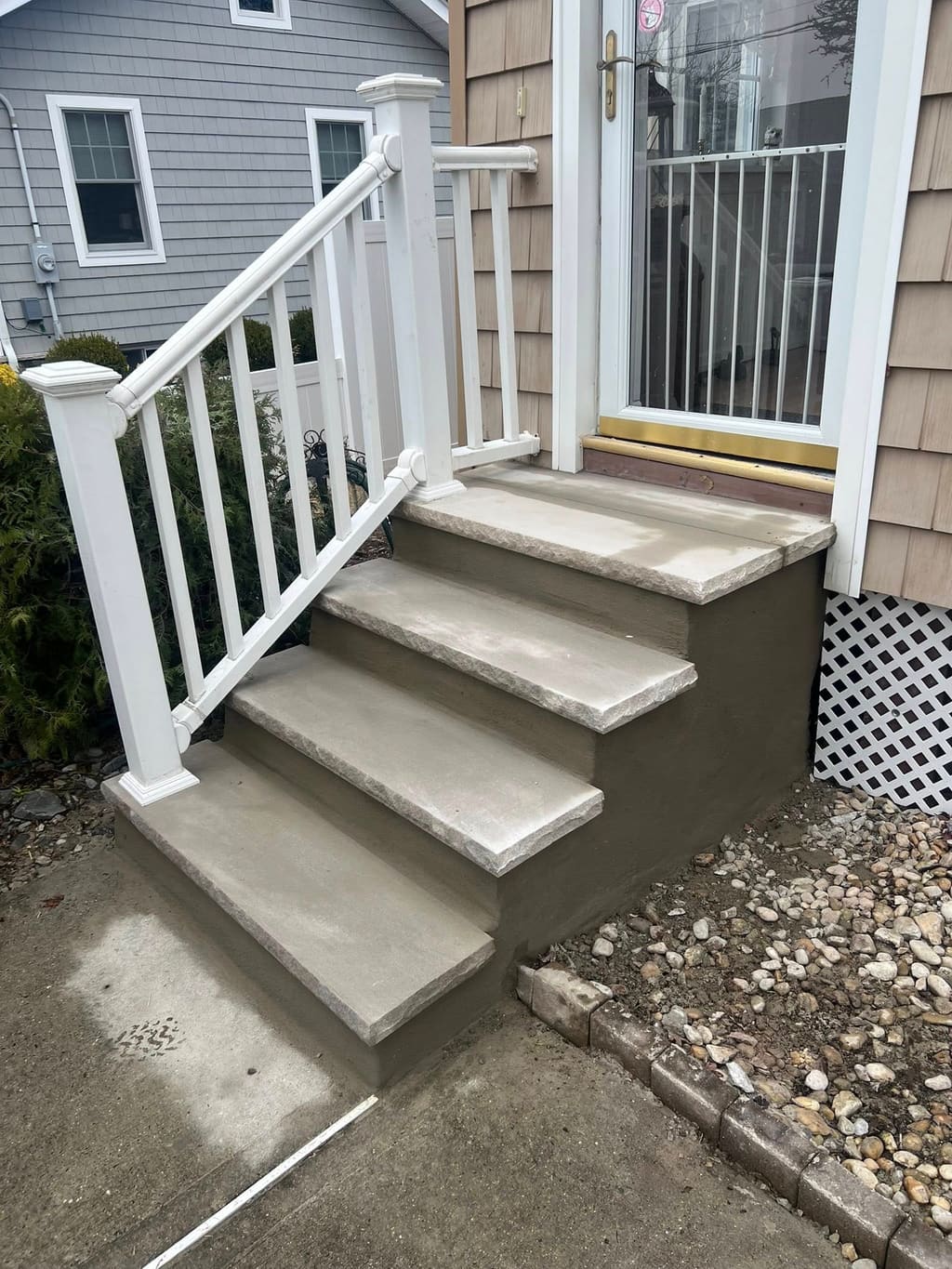 Newly built concrete front steps with bullnose treads and a white railing beside a shingled house.