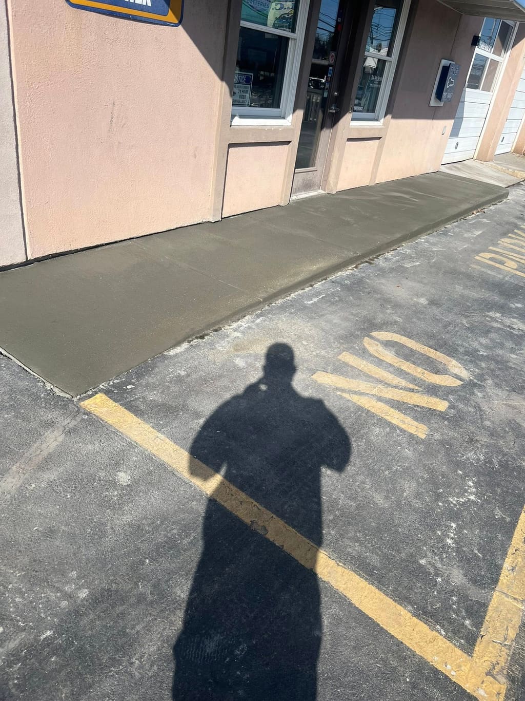 Newly poured concrete walkway running along a commercial storefront beside the parking area.