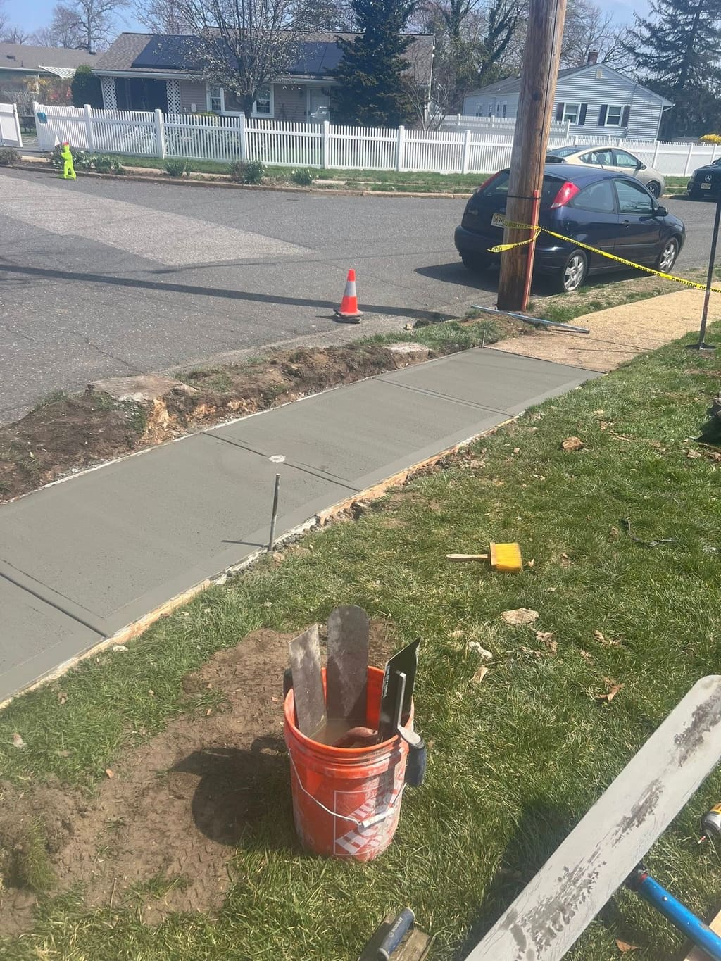 A freshly poured concrete walkway with finishing tools and a bucket at an active residential jobsite.
