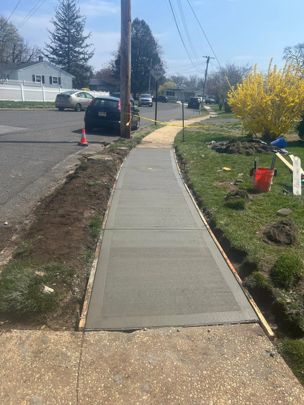 A newly poured broom-finished concrete front walkway framed by wood forms leads toward the street.