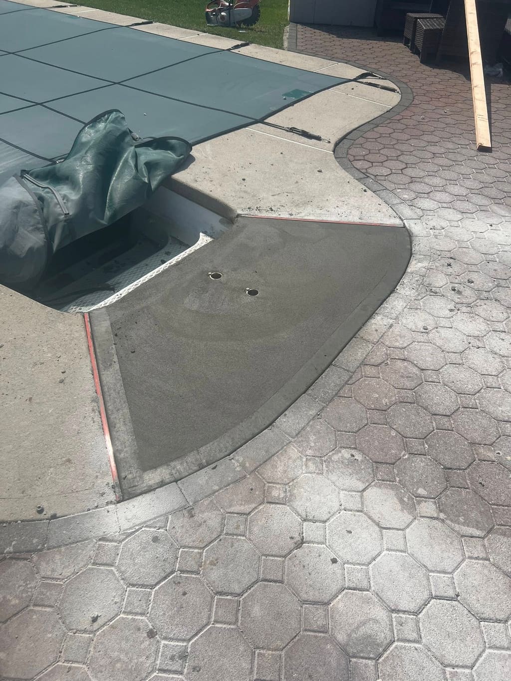 A curved concrete pool-deck section is finished alongside an interlocking paver patio near a covered pool.