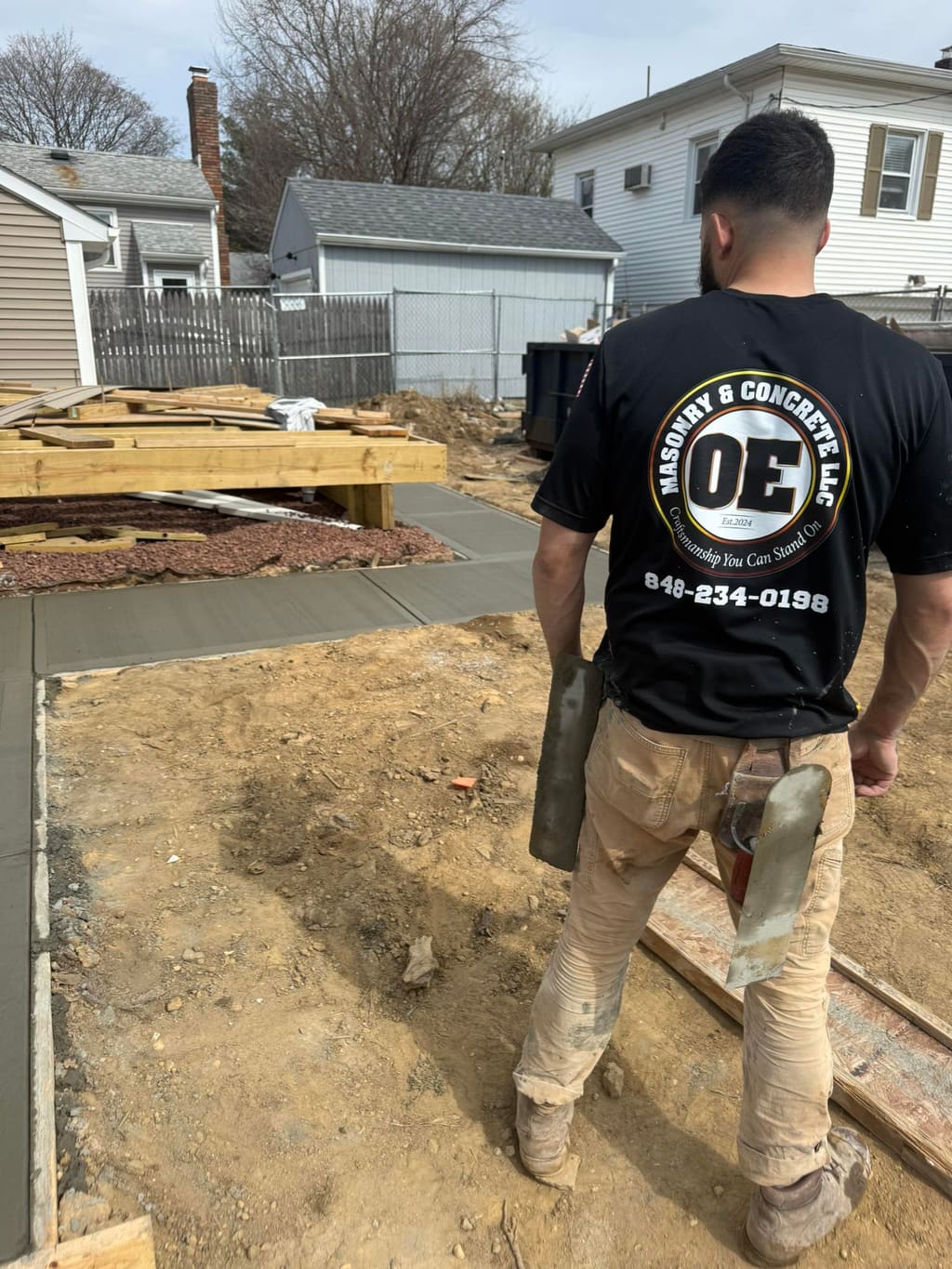 OE Masonry worker beside wood forms and a freshly poured backyard concrete slab.