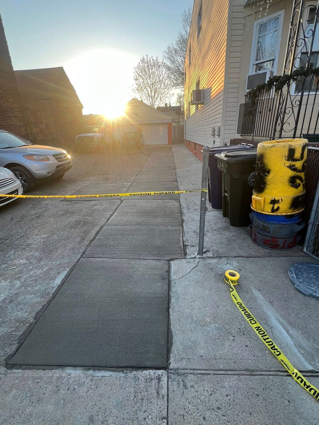 Freshly finished concrete driveway slab cordoned with caution tape under a low evening sun.