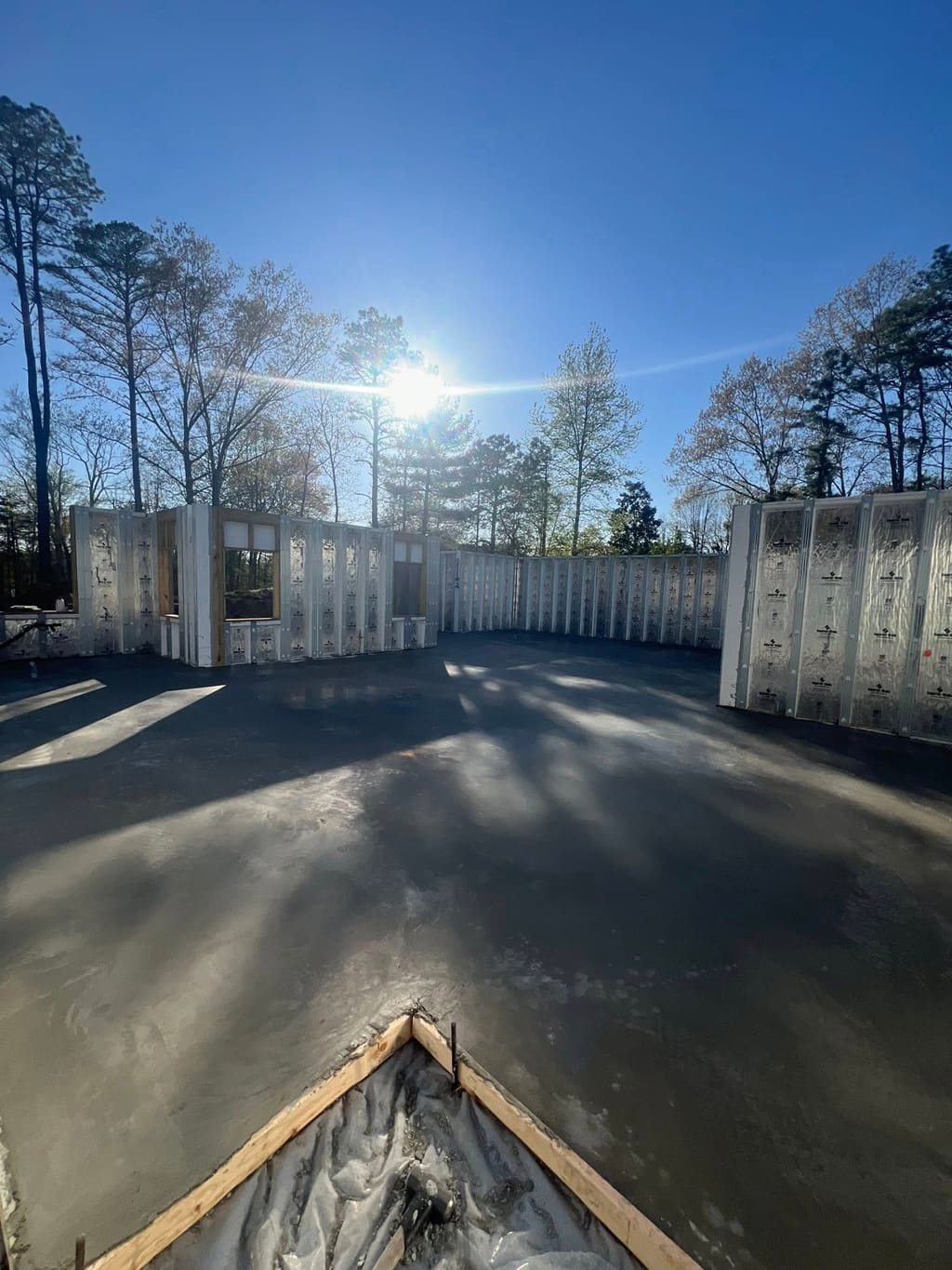 Fresh concrete foundation slab framed by insulated concrete form walls under bright sun.