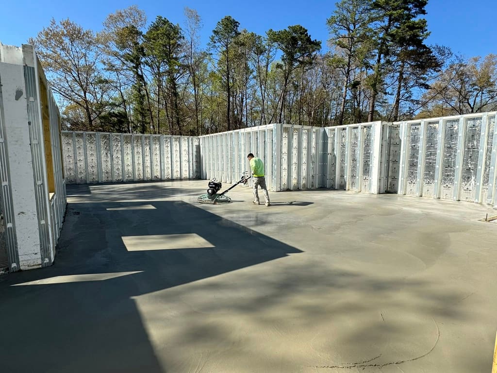 Worker power-floating a fresh concrete slab inside insulated concrete form foundation walls.