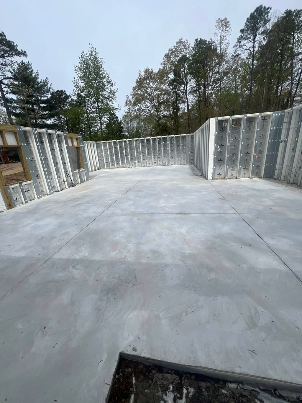 Completed concrete foundation slab enclosed by insulated concrete form walls on a treed property.