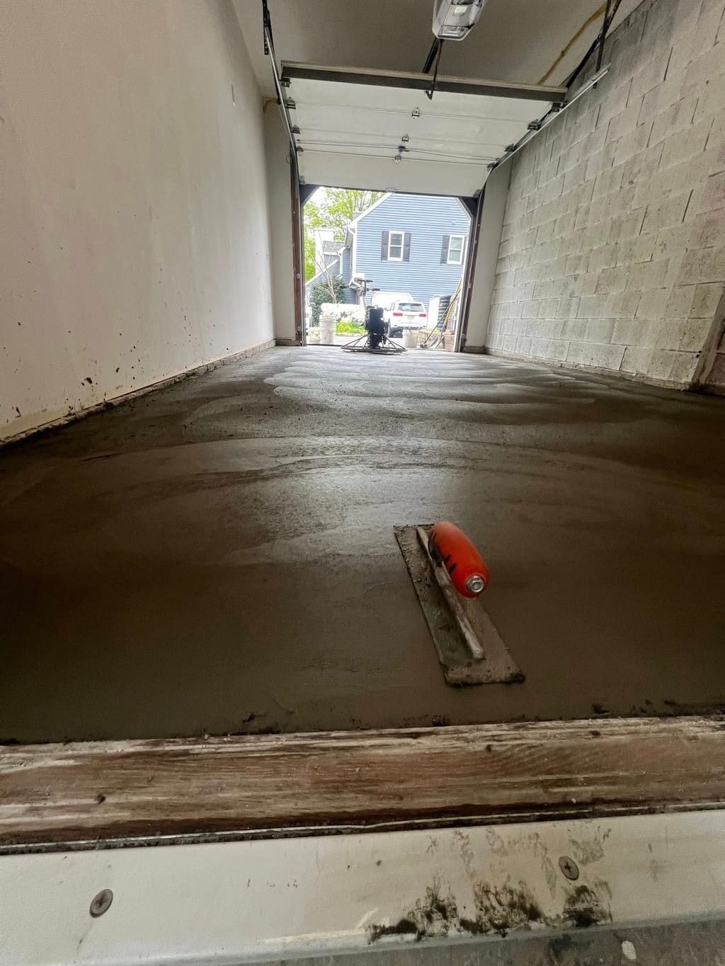 Freshly poured concrete garage floor slab with a finishing float resting on the wet surface.