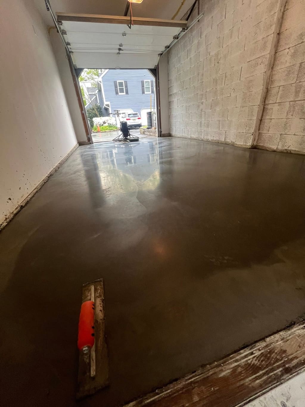 Freshly finished smooth concrete garage floor slab with a hand float and power trowel visible.