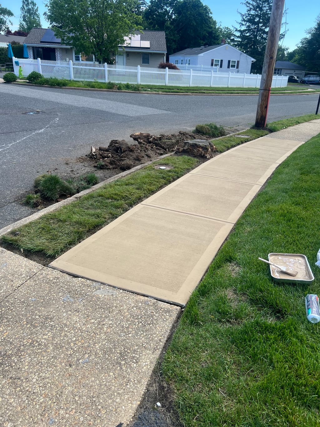 Newly poured concrete sidewalk along a street with freshly disturbed soil and a finishing float nearby.