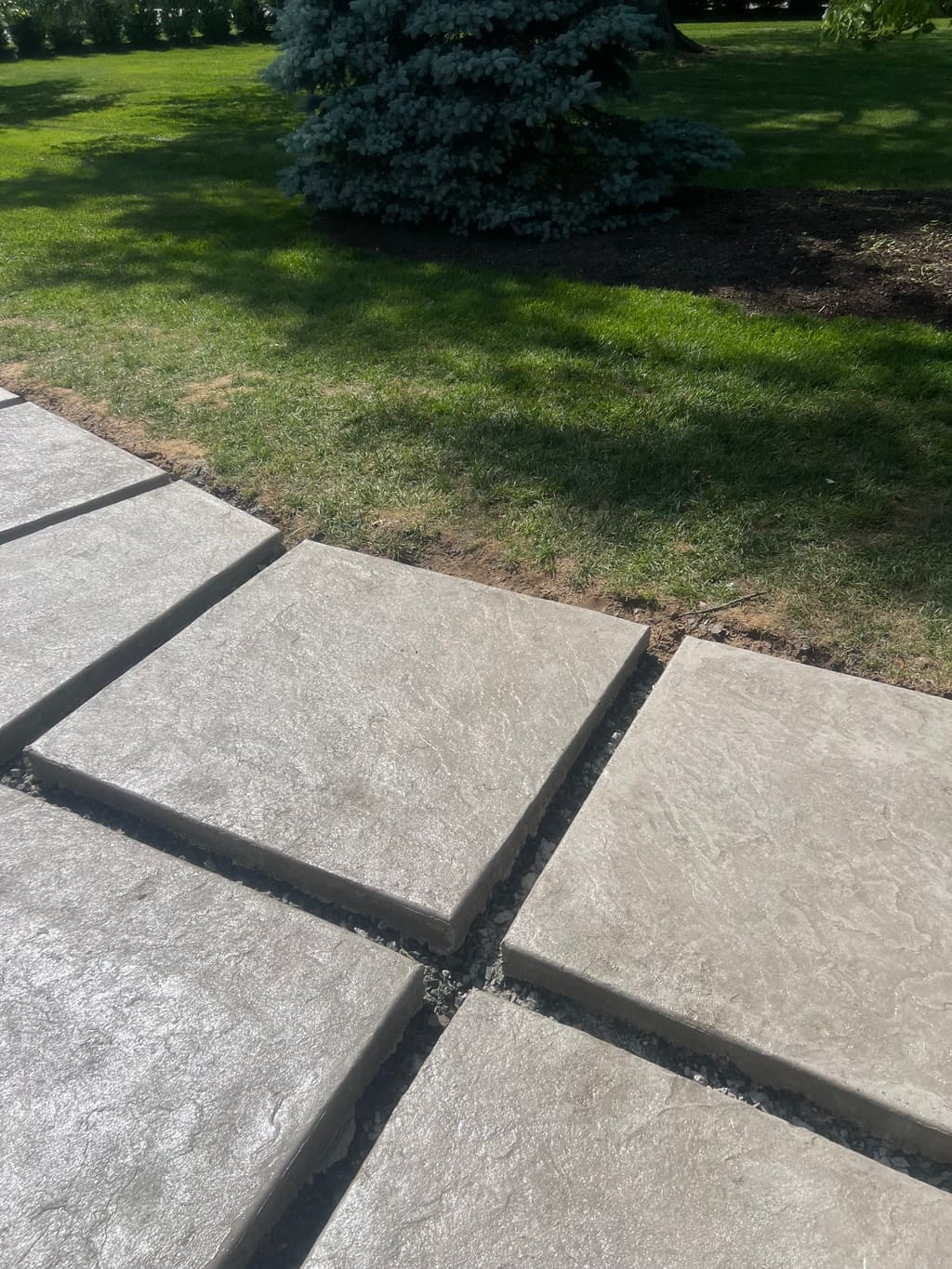 Textured stamped concrete patio with grooved joints meeting a manicured grass lawn and landscaping.