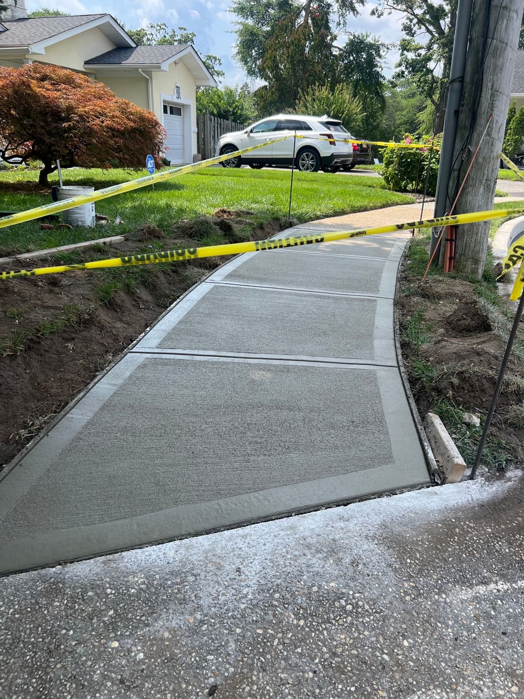 Freshly poured concrete driveway apron with a troweled border, taped off beside a lawn and garage.
