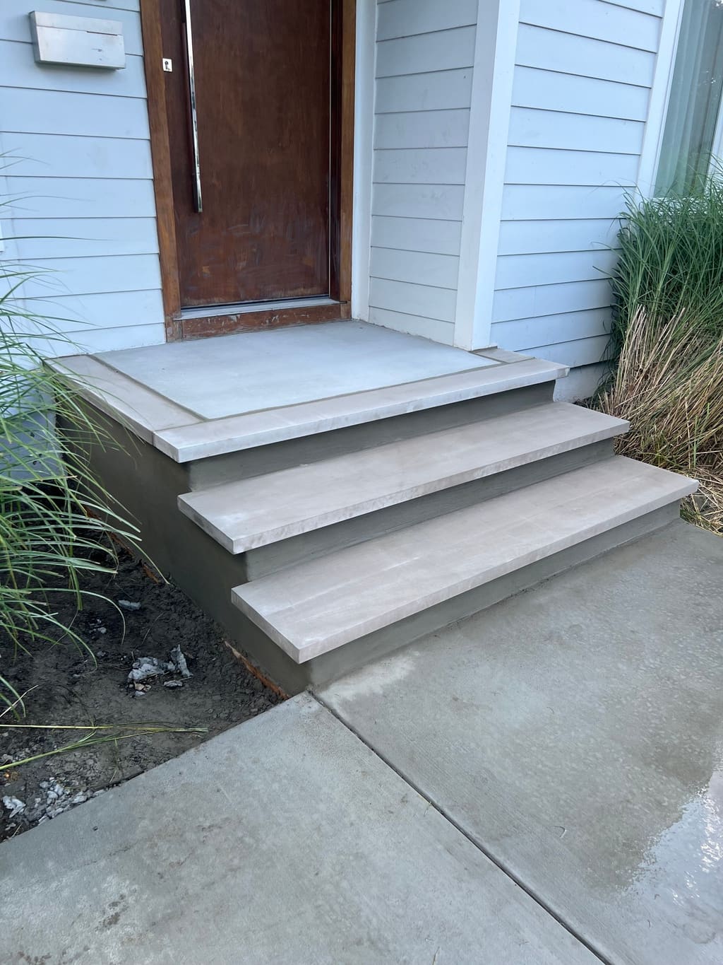 New front stoop with three natural stone treads and smooth parged risers at a blue-sided home's front door.