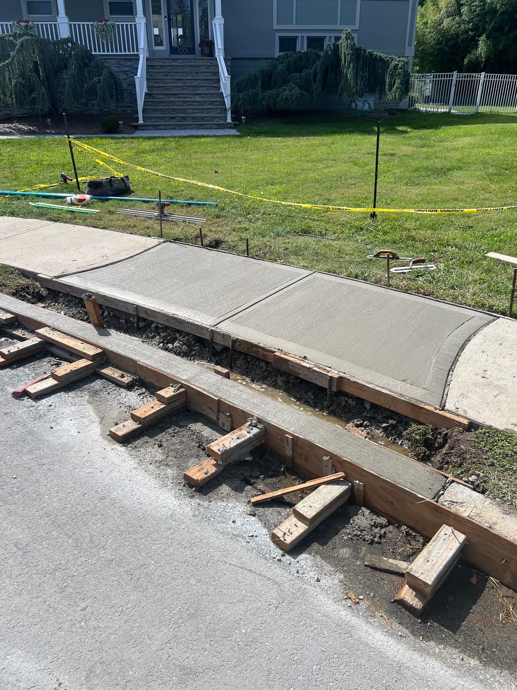 Freshly poured concrete sidewalk and curb still in wood forms along a street in front of a home.