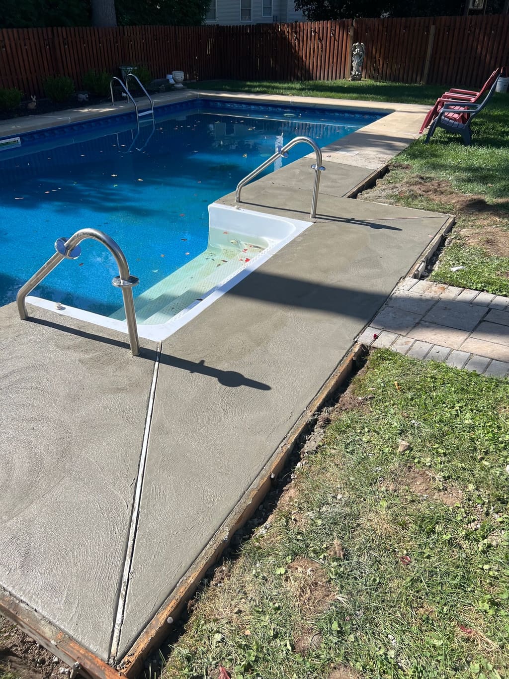 Freshly poured concrete pool deck section wrapping around the pool steps and handrails.