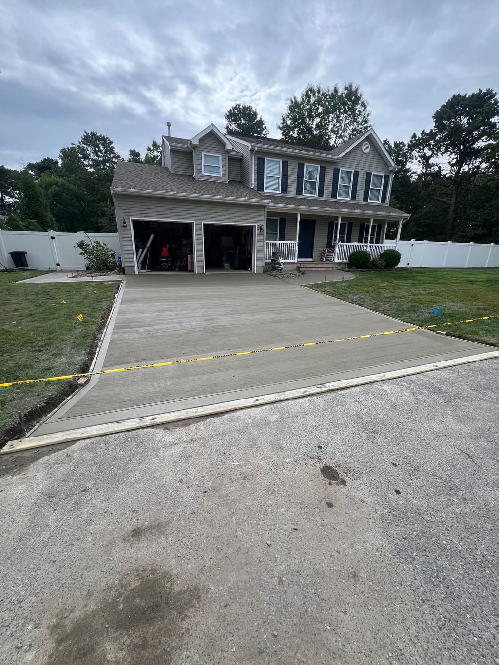 Freshly poured broom-finish concrete driveway leading up to a two-car garage on a colonial home.